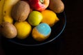 A plate with assorted whole multi-colored ripe fruits, including moldy lemon. Kiwi, apples, bananas, lemons