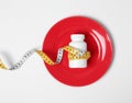 Plate with bottle of weight loss pills and measuring tape on white background Royalty Free Stock Photo