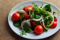 Plate with bright appetizing green salad and small red tomatoes.