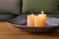 Plate with burning wax candles, water and flower petals on wooden table Royalty Free Stock Photo