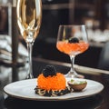 A plate with canape with red caviar and black caviar on a resatuarant table with a glass of champagne, close up. Gourmet food,