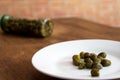 White plate with capers and glass with preserved capers