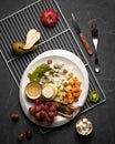 Plate with Cheese Assortment on black table with metal grill and cutlery on it. Top view. Gourmet snack from fruits