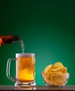 Plate with chips and light beer pouring into mug on green background Royalty Free Stock Photo