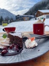 a plate of chocolate cake cherry sauce and ice cream with a bokeh background of two cups, snow and a ski lift Royalty Free Stock Photo