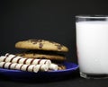 A plate of chocolate chip cookies on a blue plate with a glass of milk on a black background close-up Royalty Free Stock Photo