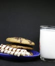 A plate of chocolate chip cookies on a blue plate with a glass of milk on a black background close-up Royalty Free Stock Photo