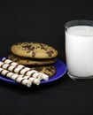 A plate of chocolate chip cookies on a blue plate with a glass of milk on a black background close-up Royalty Free Stock Photo