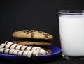 A plate of chocolate chip cookies on a blue plate with a glass of milk on a black background close-up Royalty Free Stock Photo