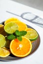 Plate of citrus fresh fruit on a white table, next to the shadow of the glass