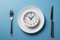 A plate with a clock, fork on the left and knife on the right, on a blue background, concept of keto diet Royalty Free Stock Photo