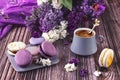 A plate with a colorful French dessert of macaroons on a wooden background and a gray cup of coffee. Purple lilac flowers Royalty Free Stock Photo