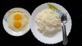 A plate of cooked steam white rice with double sunny side eggs along with fork and spoon display on black background Royalty Free Stock Photo