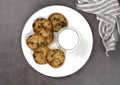 Plate with cookies, chocolate pieces, a glass of milk on a brown background, top view. Royalty Free Stock Photo