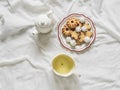 A plate of cookies, a cup of green tea, a teapot on white sheets in the bed, top view Royalty Free Stock Photo