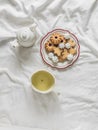 A plate of cookies, a cup of green tea, a teapot on white sheets in the bed, top view Royalty Free Stock Photo