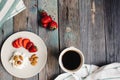 A plate with cottage cheese, strawberries and nuts, a cup of coffee and towels on a wooden table