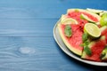 Plate with cut juicy watermelon and lime on blue wooden table, space for text Royalty Free Stock Photo