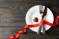 Plate with cutlery, ribbon and chocolate heart on wooden background