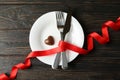 Plate with cutlery, ribbon and chocolate heart on wooden background