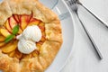 Plate with delicious peach galette and ice-cream on white wooden table