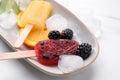 Plate of delicious popsicles, ice cubes and fresh fruits on white table Royalty Free Stock Photo