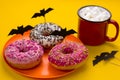 Plate with donuts decorated with paper cut bats and a mug of cocoa with marshmallows on the table at a Halloween party