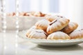 A plate of dusted pastries filled with sweet cream or fruit presented on a table with a reflective light table surface. Homemade