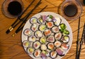 A plate filled with various sushi rolls alongside a pair of chopsticks placed on a wooden table Royalty Free Stock Photo