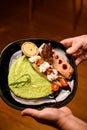 plate with fish dish garnished with cheese, vegetables and greens sauce in male hands