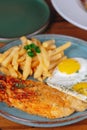 A plate of food with a fried egg, a piece of fish, and some french fries Royalty Free Stock Photo