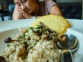 A plate of food made of rice, mushrooms, and meat in front of a woman in the background losing appetite