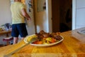 A plate of food on the table. In the background, a man opened the refrigerator