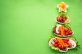 Plate in the form of a Christmas tree with vegetables, fruits, mushrooms and berries.Green background. The concept of vegetarian