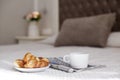 A plate of fresh croissants, a Cup of coffee, and a morning newspaper lie on the bed in the bright room. Romantic breakfast. Space Royalty Free Stock Photo