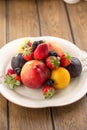 Plate with fresh whole berries and fruits peach, plum, strawberry and blackberry on wooden table Royalty Free Stock Photo
