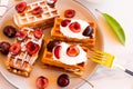 A plate with freshly soft Belgian waffles and cherries with cream on a white table