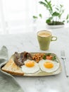 Plate of fried eggs, bacon, baked beans, fresh toast and cup of coffee on white marble table in front of window. English Royalty Free Stock Photo