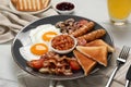 Plate of fried eggs, mushrooms, beans, tomatoes, bacon, sausages and toasts on white marble table, closeup. Traditional Royalty Free Stock Photo