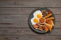 Plate of fried eggs, mushrooms, beans, tomatoes, bacon, sausages and toasts on wooden table, top view with space for text. Royalty Free Stock Photo