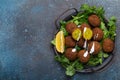 Plate of fried falafel balls served with fresh green cilantro and lemon top view on rustic concrete background