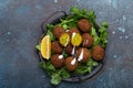 Plate of fried falafel balls served with fresh green cilantro and lemon, top view on rustic concrete background