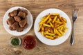 Plate with meatballs, bowls with dried parsley and ketchup, pieces of fried potato in white plate, fork on table. Top view