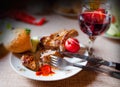 A plate with fried steak, radish, cucumber and bread near a glass with ruby wine