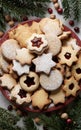 A plate full of assorted cookies, including star and round shapes, some dusted with powdered sugar and others filled with red jam