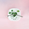 Plate with green leaves hearts and silverware. Valentine design aesthetic on a pink background.Love abstract Royalty Free Stock Photo