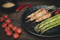 Plate with grilled chicken skewers, green asparagus and peanut sauce on dark wood Royalty Free Stock Photo
