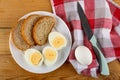 Plate with halves of boiled eggs, slices of bread, egg, knife on napkin on wooden table. Top view Royalty Free Stock Photo