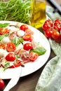 Plate of healthy classic delicious caprese salad with ripe tomatoes and mozzarella cheese with fresh basil leaves on white wooden Royalty Free Stock Photo
