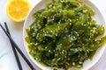 Plate with healthy seaweed salad, lemon and chopsticks on a light background. Close-up. Japanese traditional food